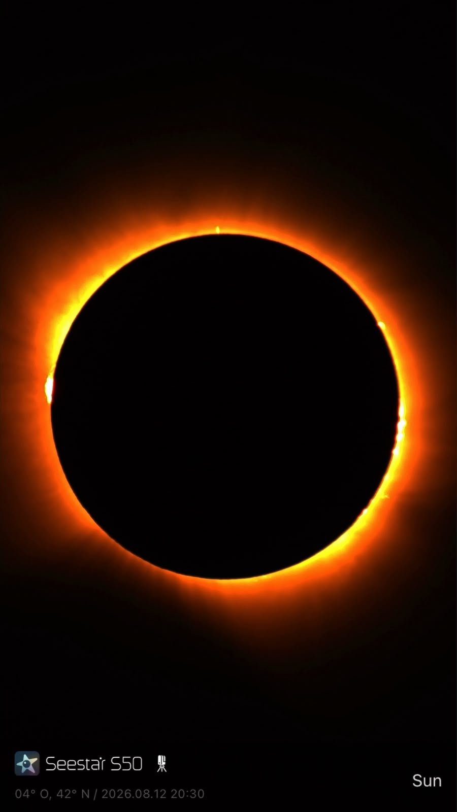 Image de l’éclipse au voisinage de la totalité avec le disque lunaire noir et un contour lumineux orangé, portant la signature Seestar S50