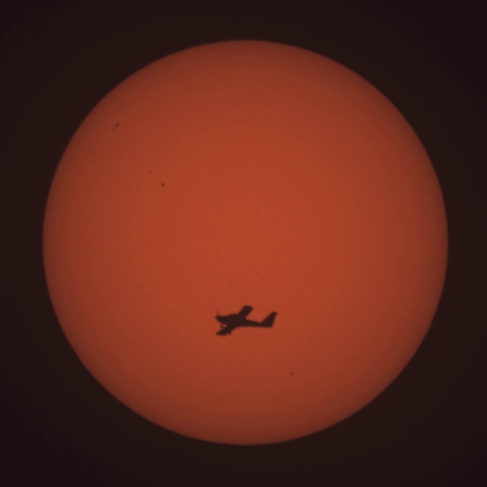 Silhouette d’un avion capturée au Seestar S50 devant le disque solaire orangé, avec des taches solaires visibles